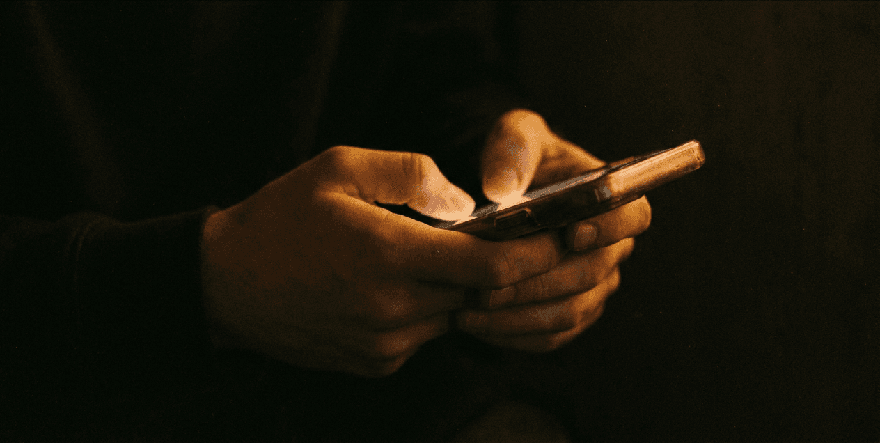 A pair of hands holding a phone in low light, the screen glowing warm.